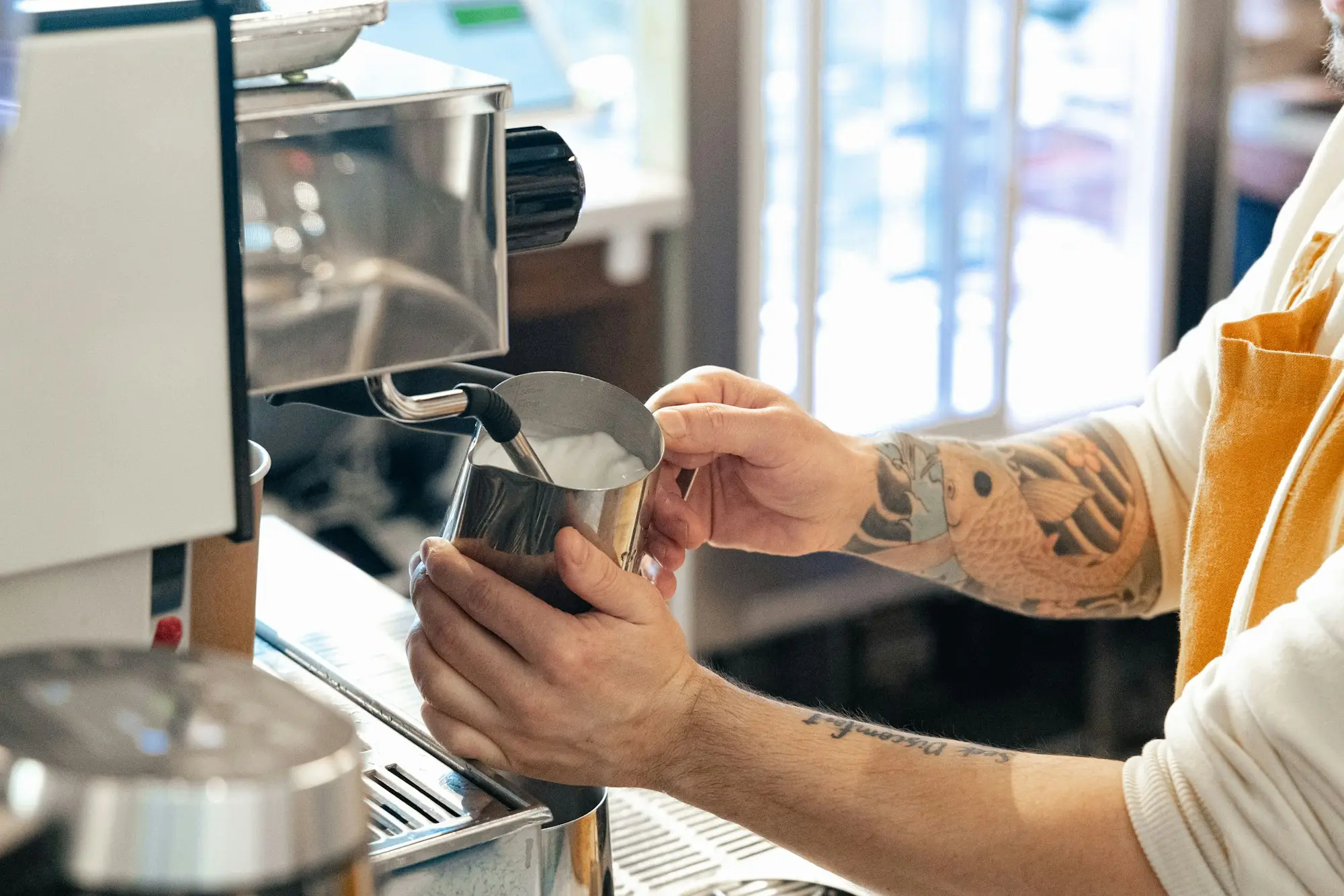 Café owner pouring milk at the espresso machine during a busy morning service