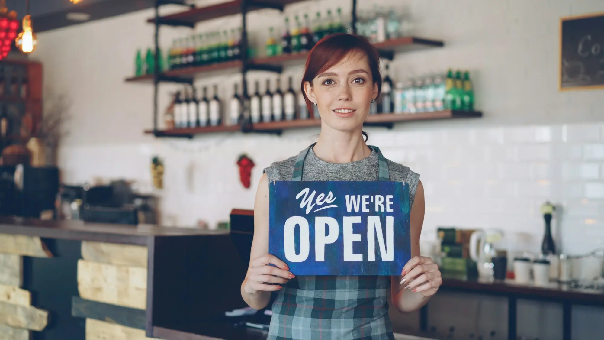 Shop owner holding a "Yes, we're open" sign at the counter of her store